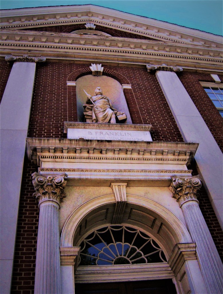 A photograph of a statue inset into a wall brick wall of a neoclassical building.